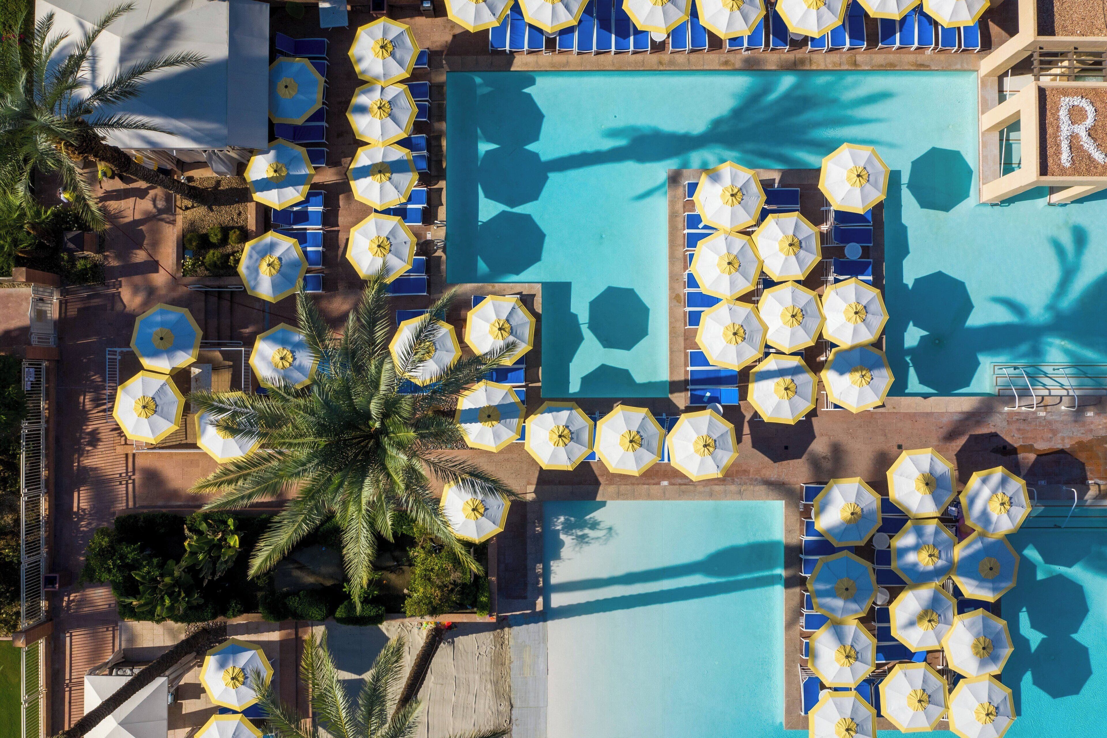 Un área de piscina en la azotea con múltiples sombrillas y sillones de descanso alrededor de la piscina.