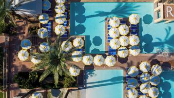 Un área de piscina en la azotea con múltiples sombrillas y sillones de descanso alrededor de la piscina.