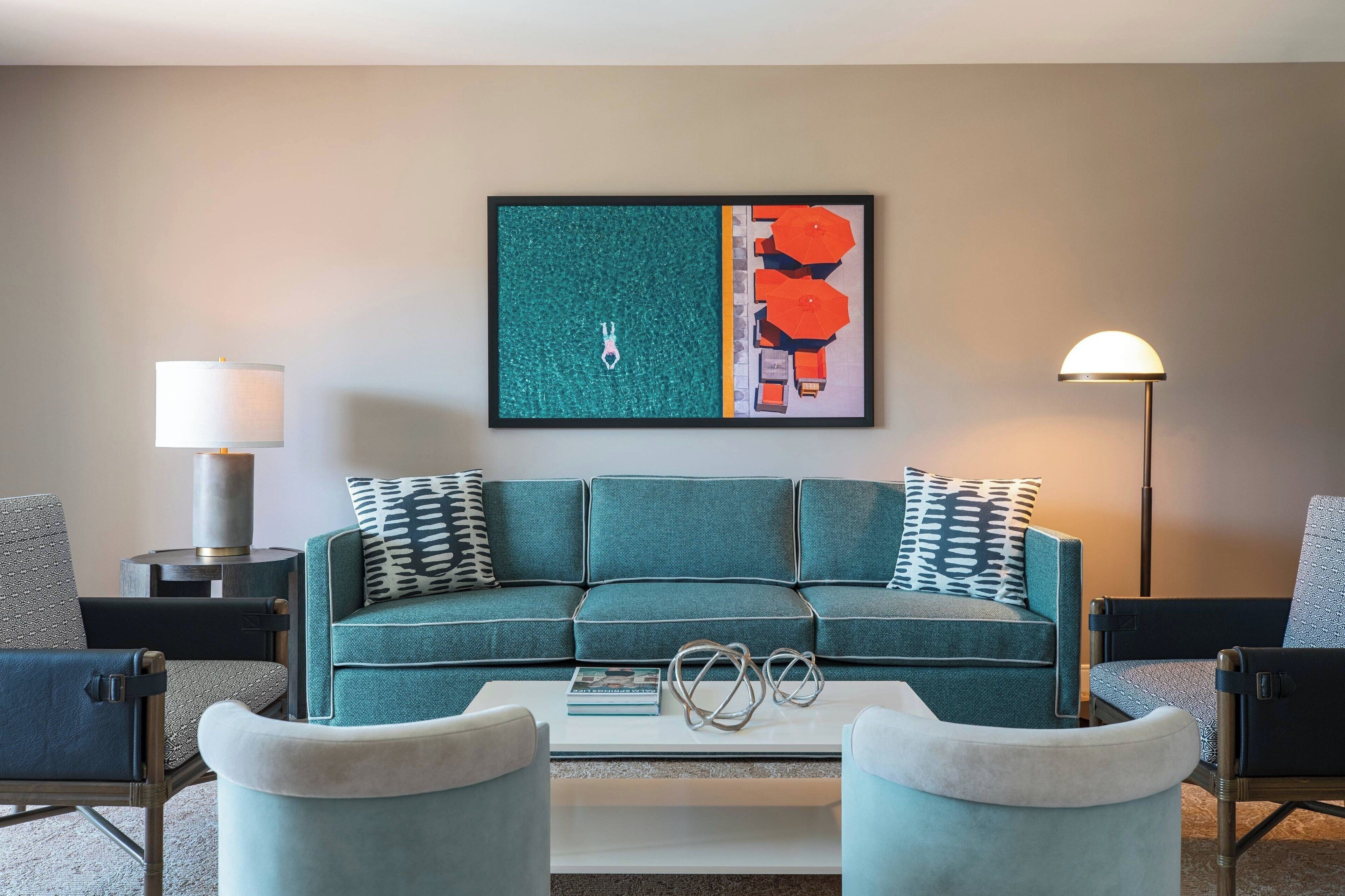 Un salon moderne avec un canapé de couleur turquoise, deux fauteuils, une table basse et un tableau abstrait encadré.