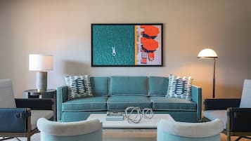 Un salon moderne avec un canapé de couleur turquoise, deux fauteuils, une table basse et un tableau abstrait encadré.
