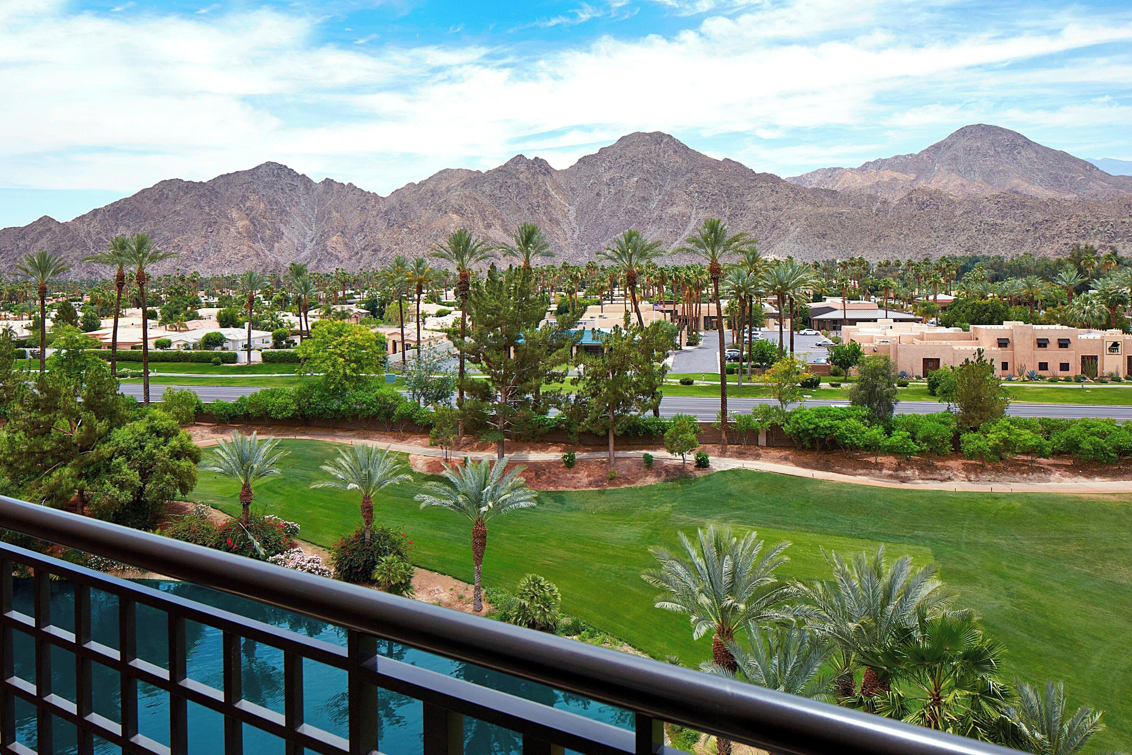 A resort with a pool, palm trees, and mountains in the background.