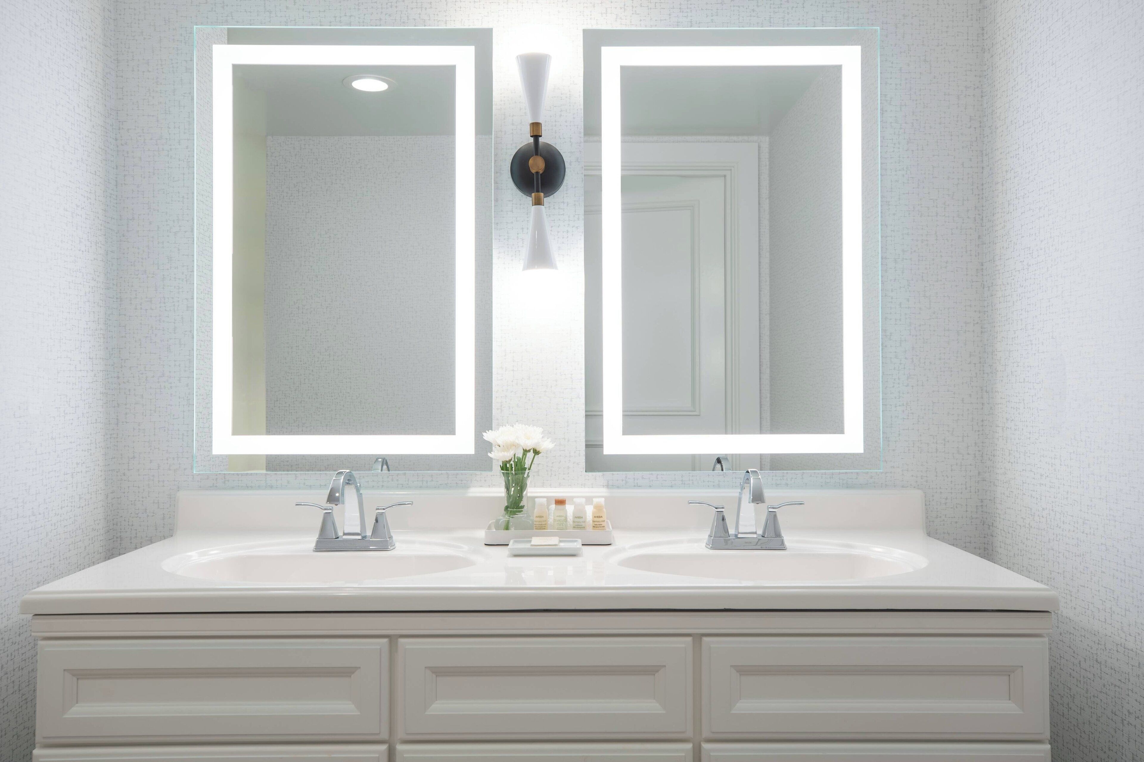 A bathroom with a double sink vanity, two large mirrors, and a wall-mounted light fixture.