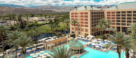 A hotel with a large pool, palm trees, and a mountainous backdrop.