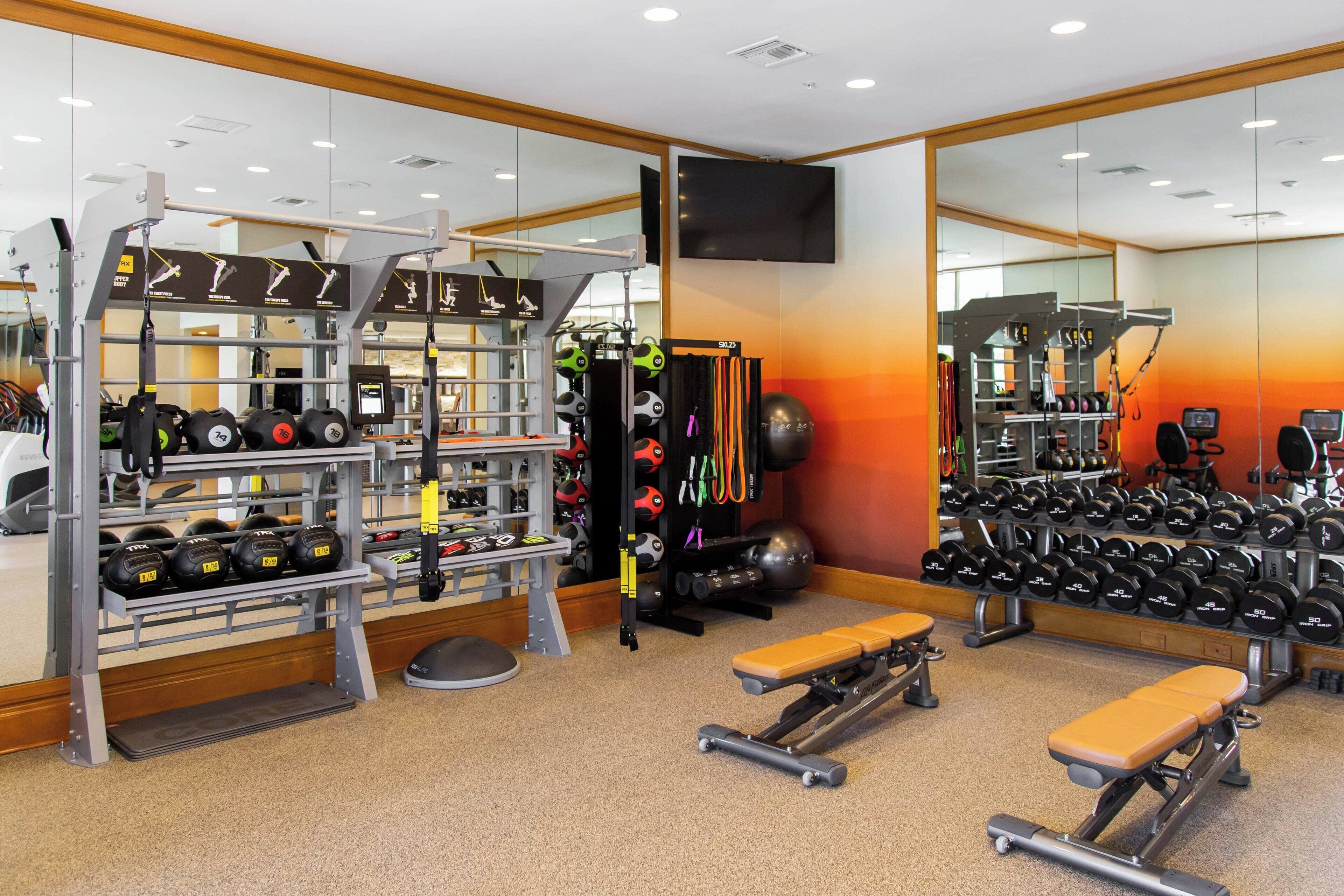 A gym with weightlifting equipment, benches, and a mirrored wall.