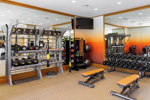 A gym with weightlifting equipment, benches, and a mirrored wall.