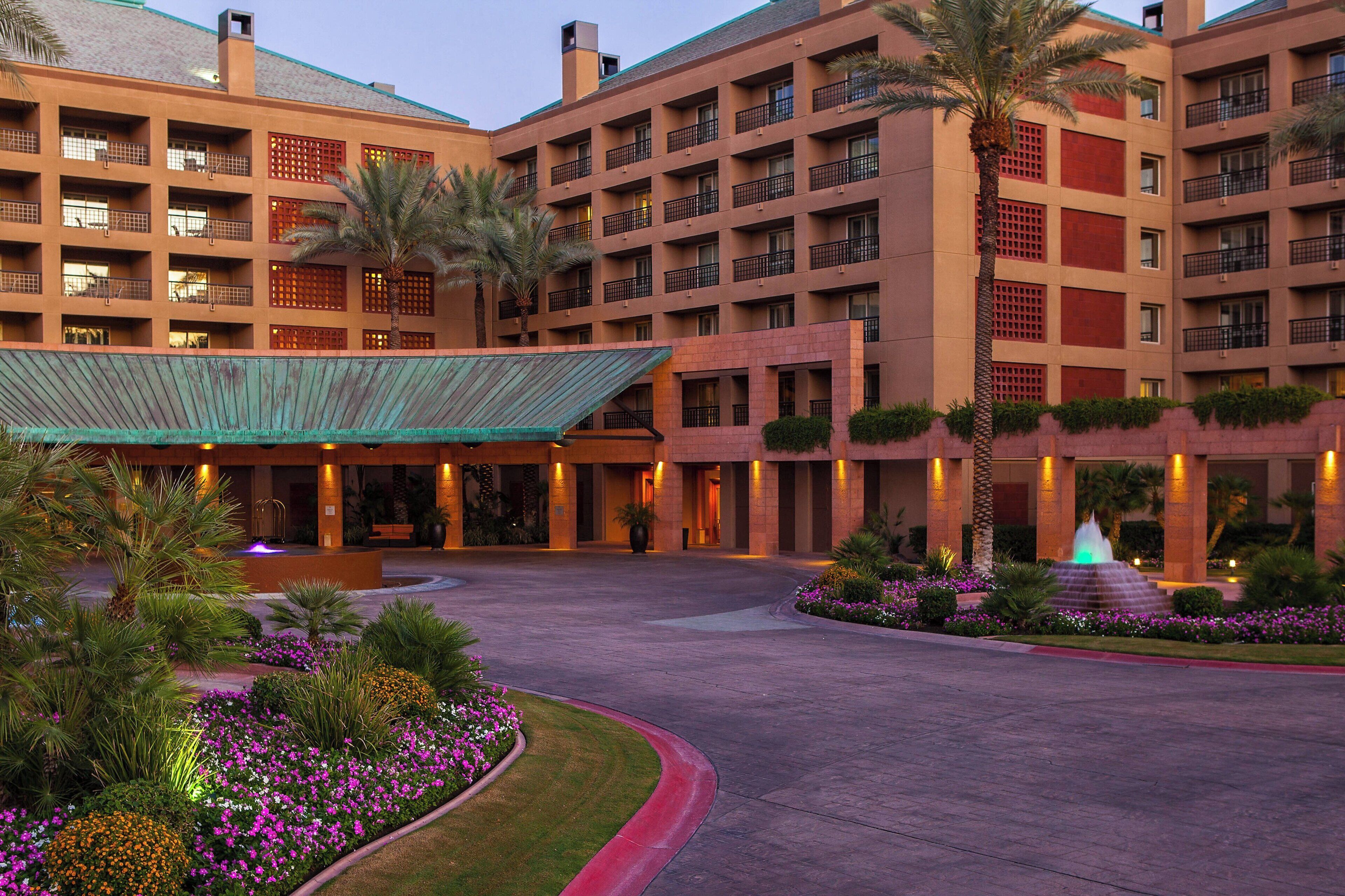 A multi-story hotel with a central courtyard, palm trees, and a fountain.
