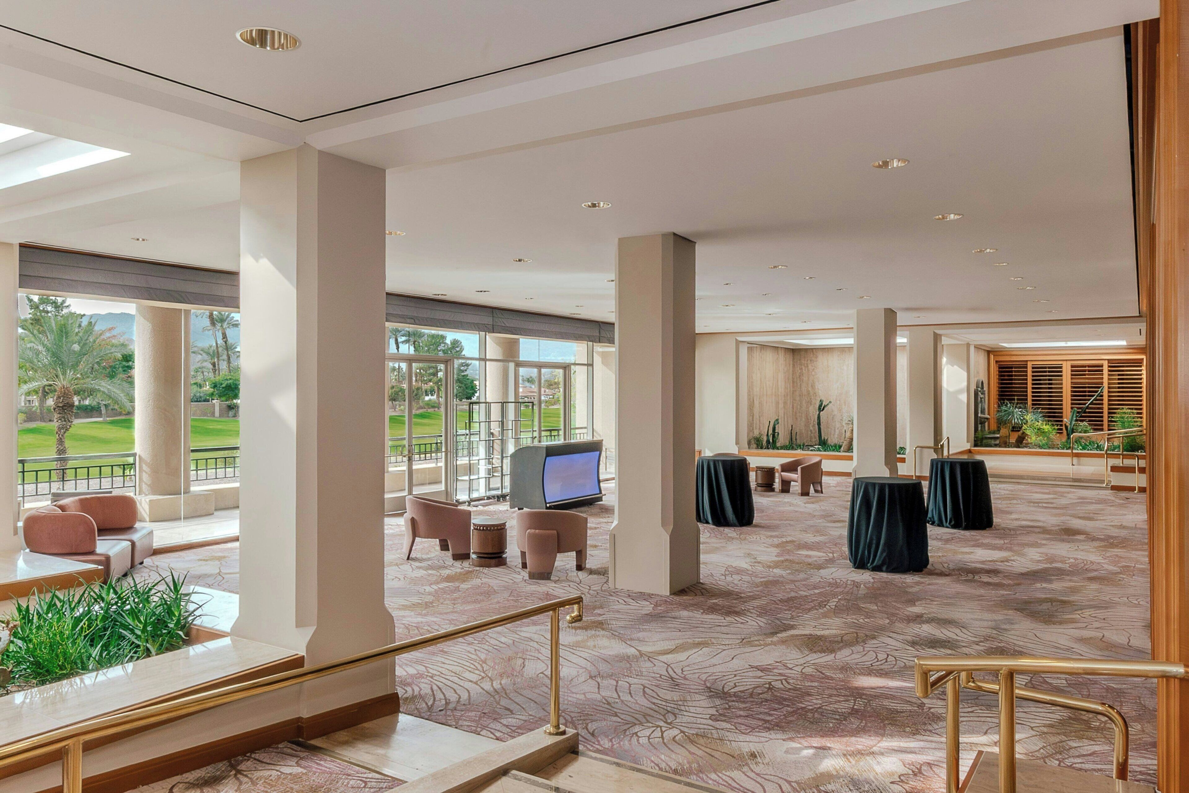 Eine geräumige Hotelhalle mit hoher Decke, großen Fenstern und Blick auf einen Golfplatz.