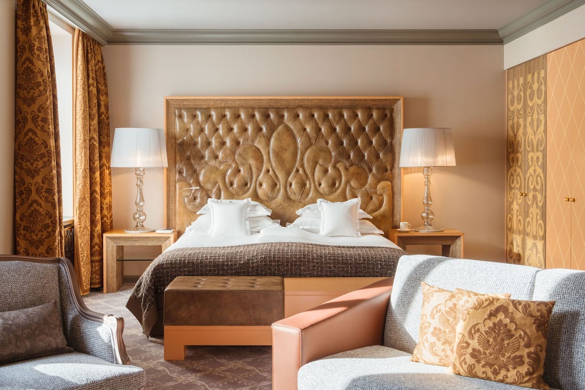 A hotel room with a large bed, two bedside tables with lamps, a sofa, and a patterned wall.