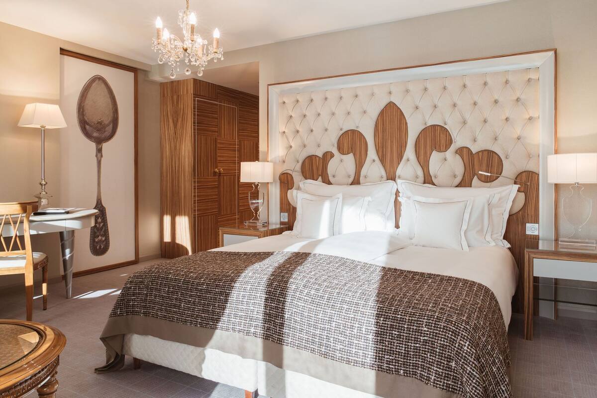 A hotel room with a large bed, a chandelier, and a wooden headboard.