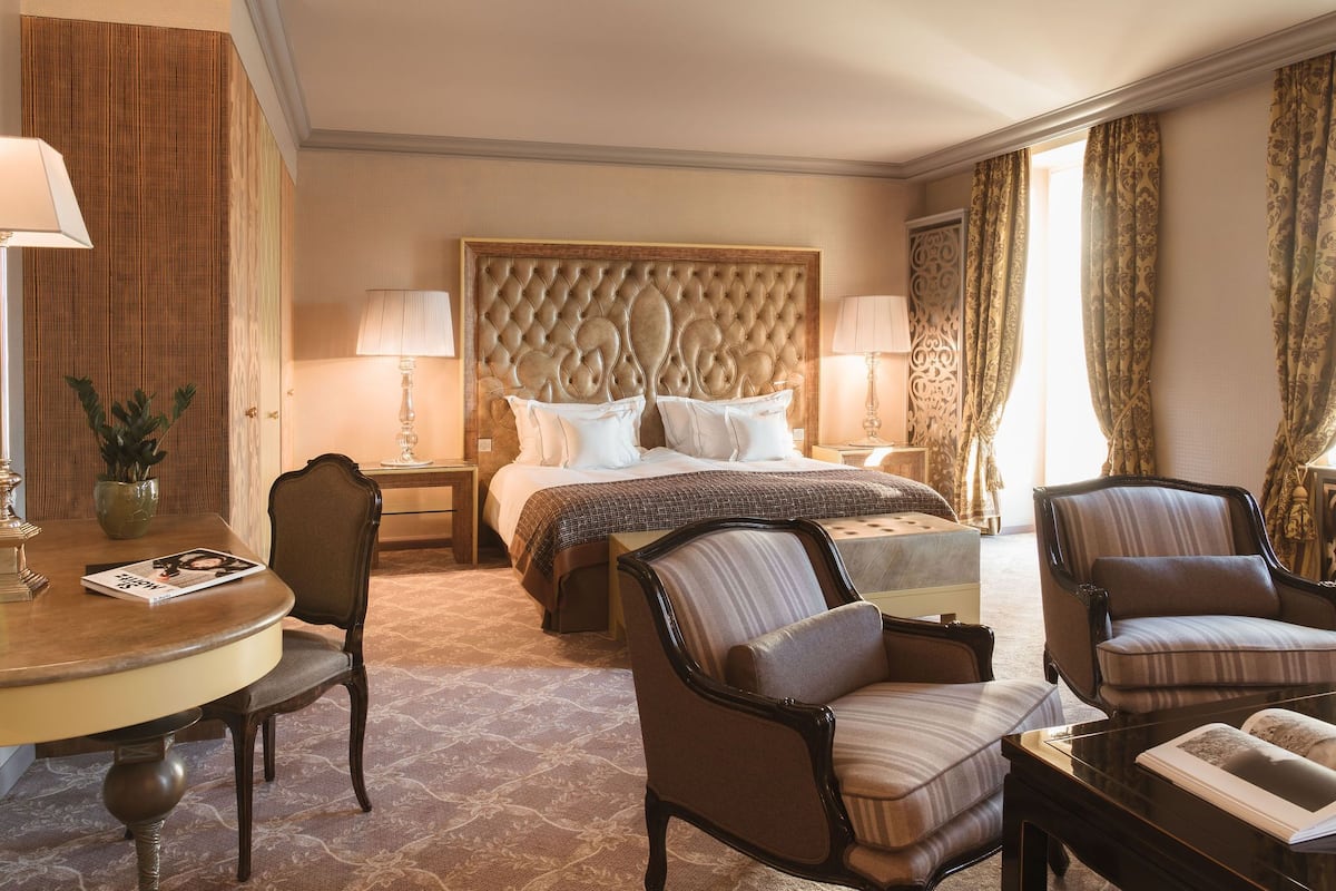 A hotel room with a large bed, two bedside tables, a round dining table, and two armchairs.