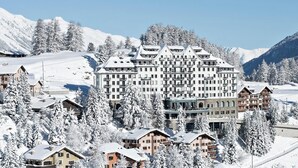 A large hotel with multiple floors and balconies, surrounded by snow-covered trees and mountains.