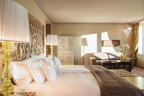 A hotel room with a large bed, two bedside tables, a sofa, a chandelier, and a view of the outdoors.