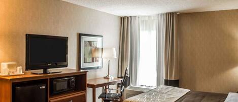 Una habitación de hotel con una cama, un escritorio con computadora, televisión y minibar.