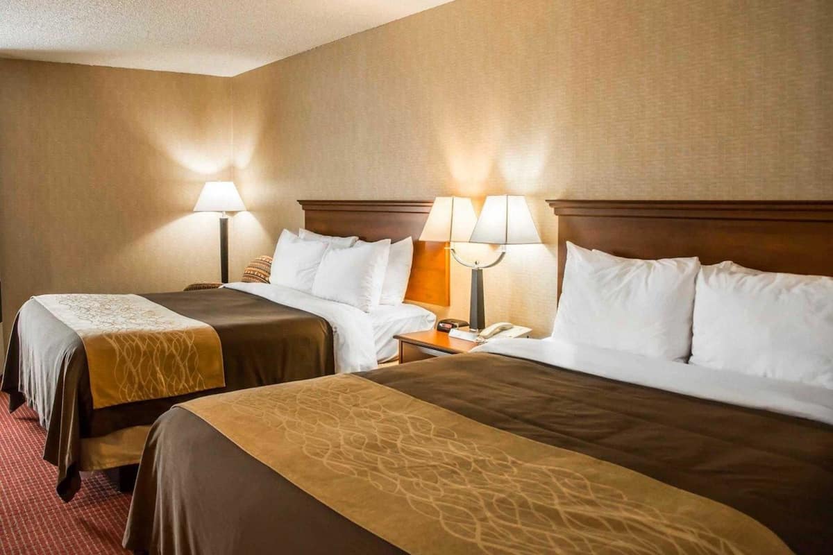 A hotel room with two beds, each with a wooden headboard, a nightstand, and a lamp.