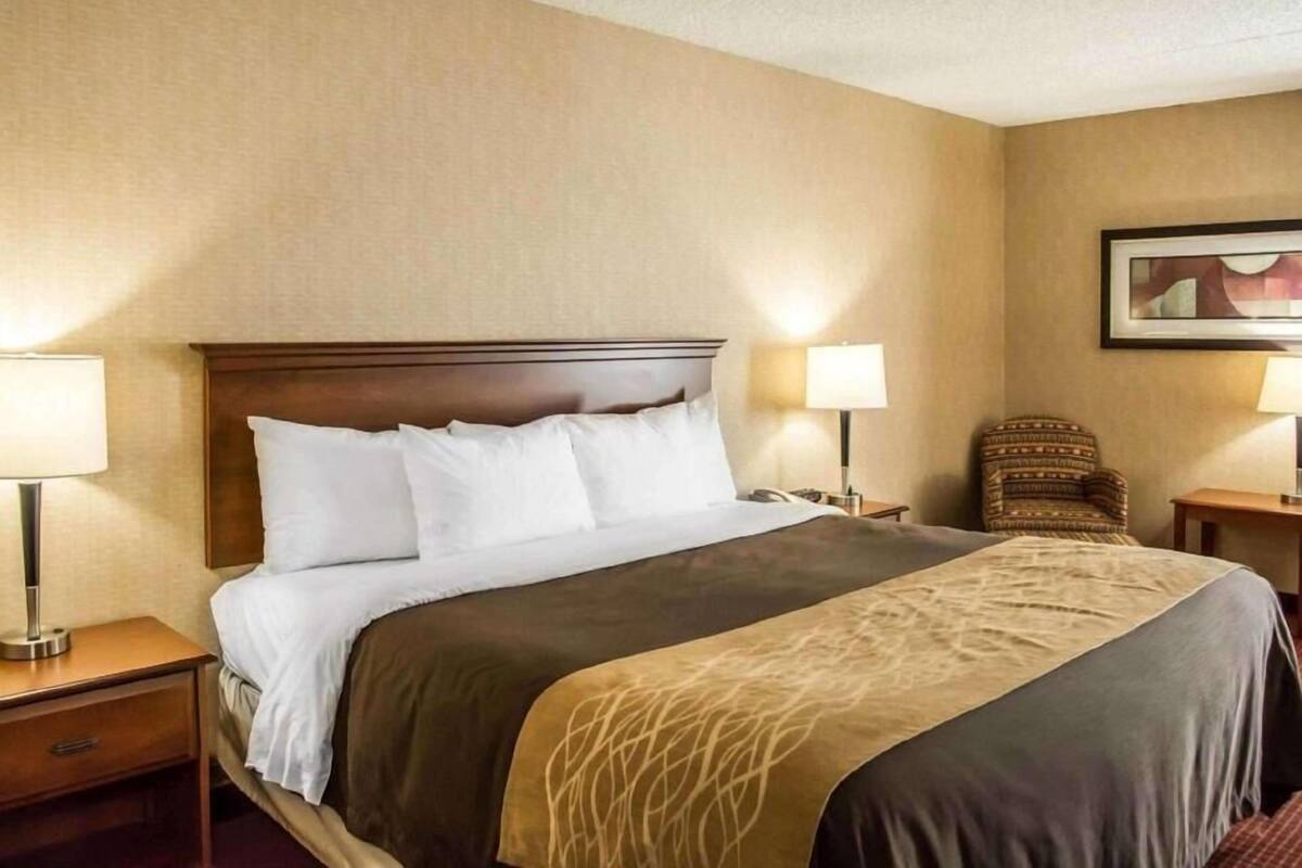 A hotel room with a large bed, two bedside tables with lamps, a chair, and a framed picture on the wall.
