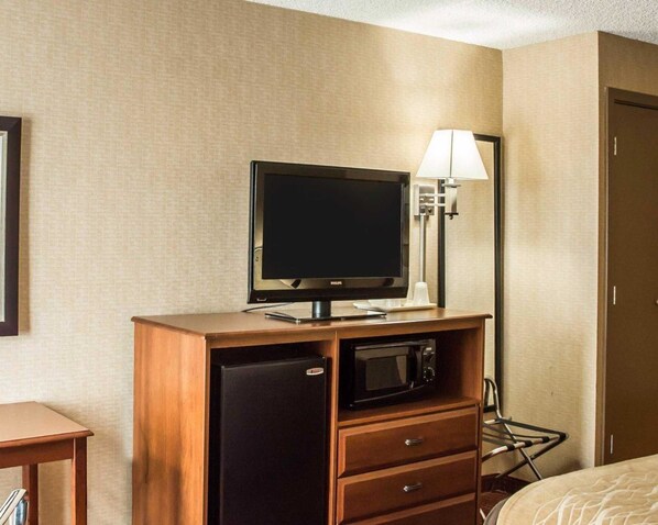 A hotel room with a television on a wooden stand, a microwave, a small refrigerator, a lamp, and a bed. - Quality Inn Springboro West (Springboro)