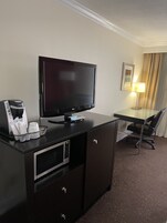 Habitación de hotel con televisión de pantalla plana, cafetera, escritorio, silla y lámpara.