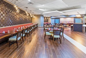 A restaurant with multiple dining tables and chairs, a patterned wall, and hanging light fixtures.