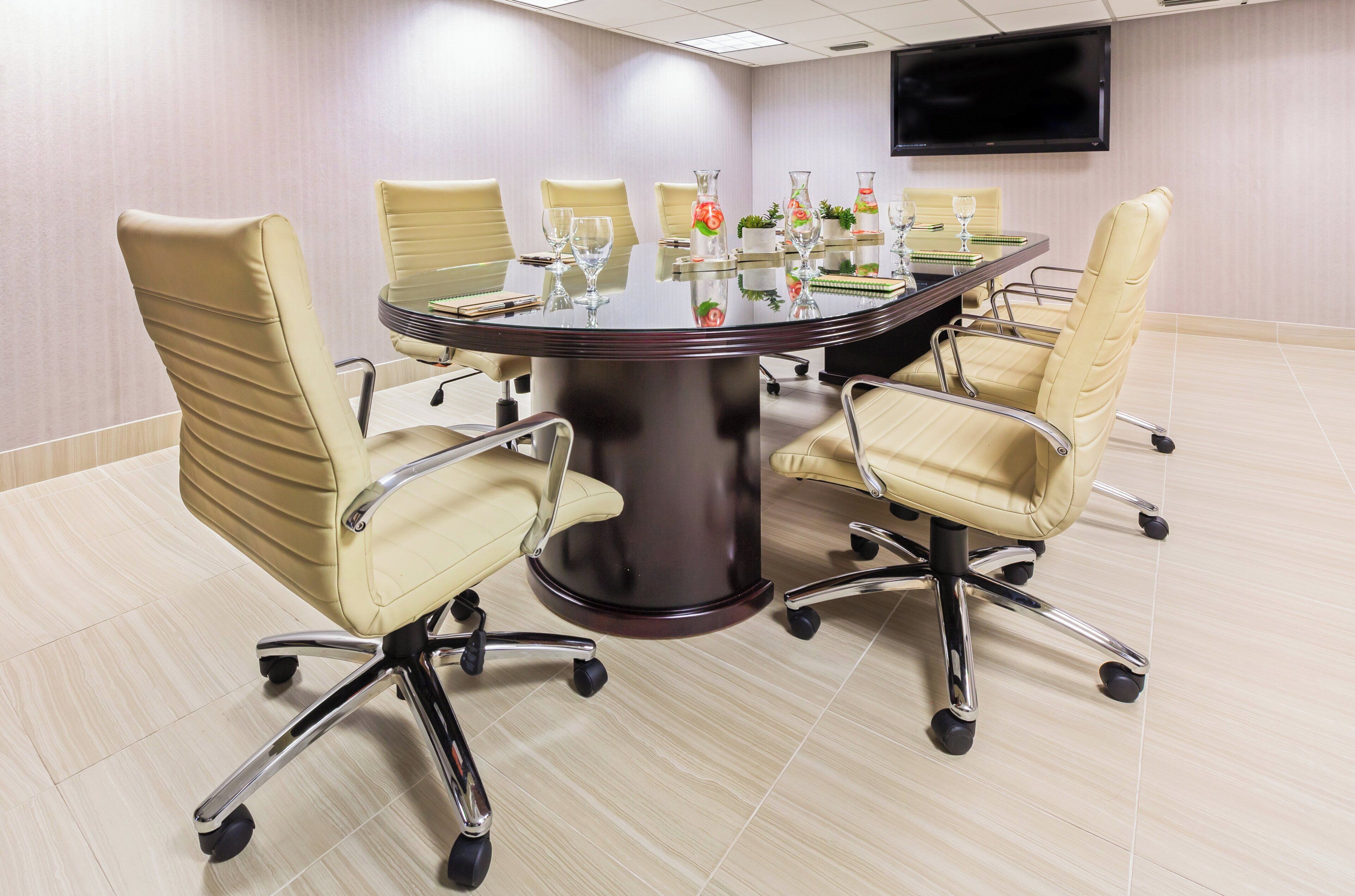 A conference room with a round table, six chairs, and a flat-screen TV on the wall.