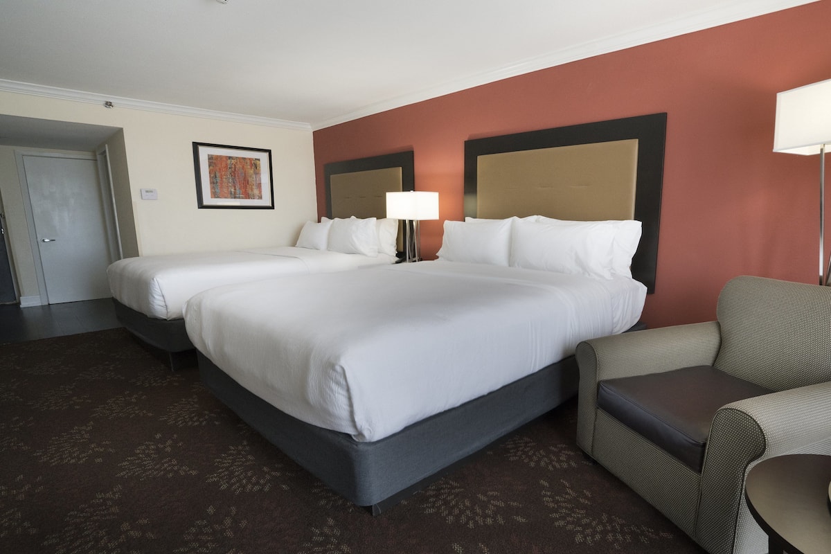 Una habitación de hotel con una cama grande, una silla, una lámpara y un cuadro en la pared.