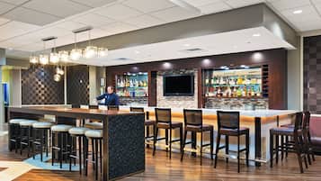 A bar area with a bartender, stools, and a variety of liquor bottles.