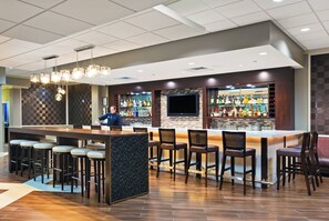 A bar area with a bartender, stools, and a variety of liquor bottles. - Holiday Inn Tyler-Conference Center by IHG (Tyler)