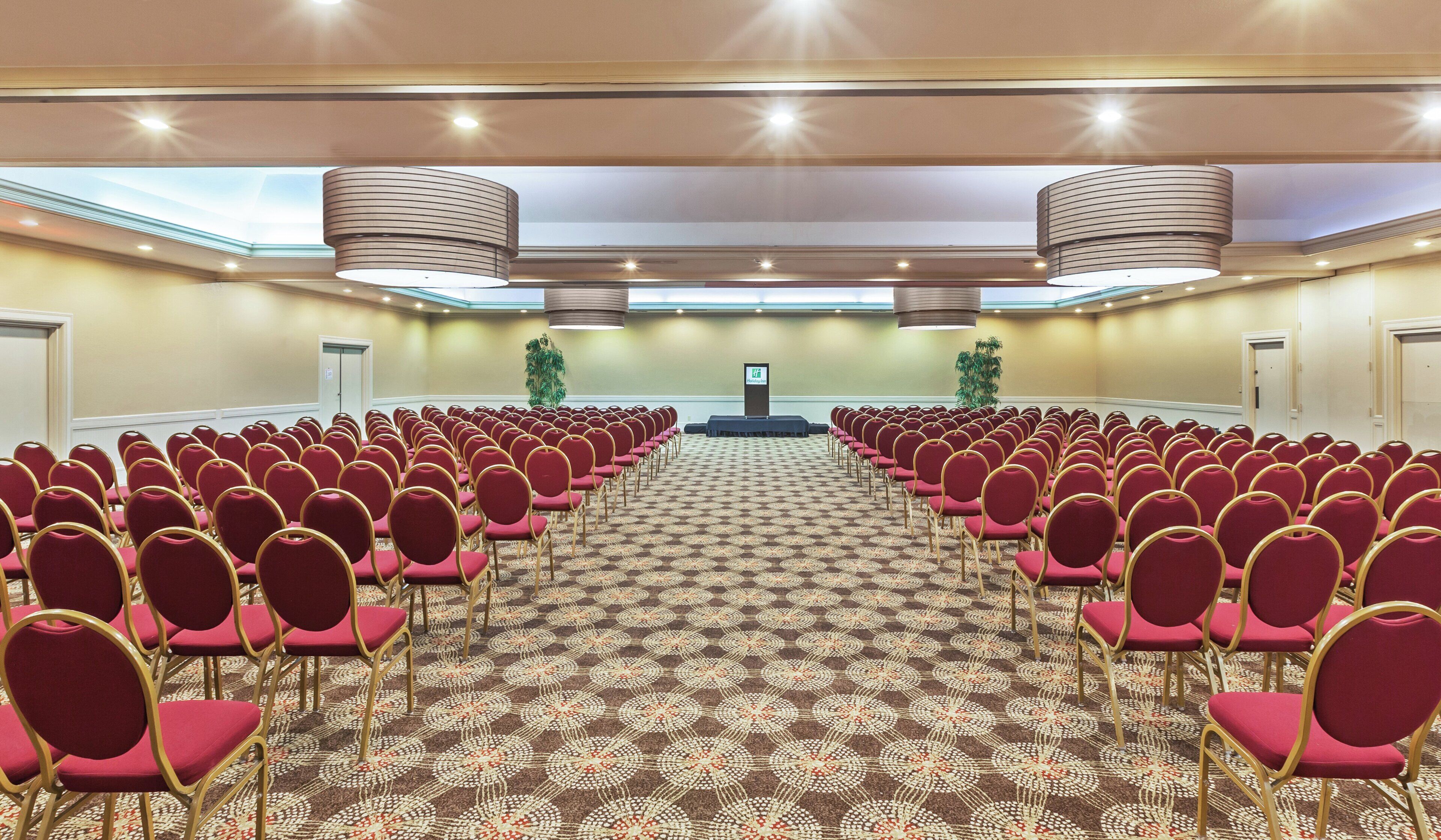 A conference room with rows of chairs, a podium, and a patterned carpet.