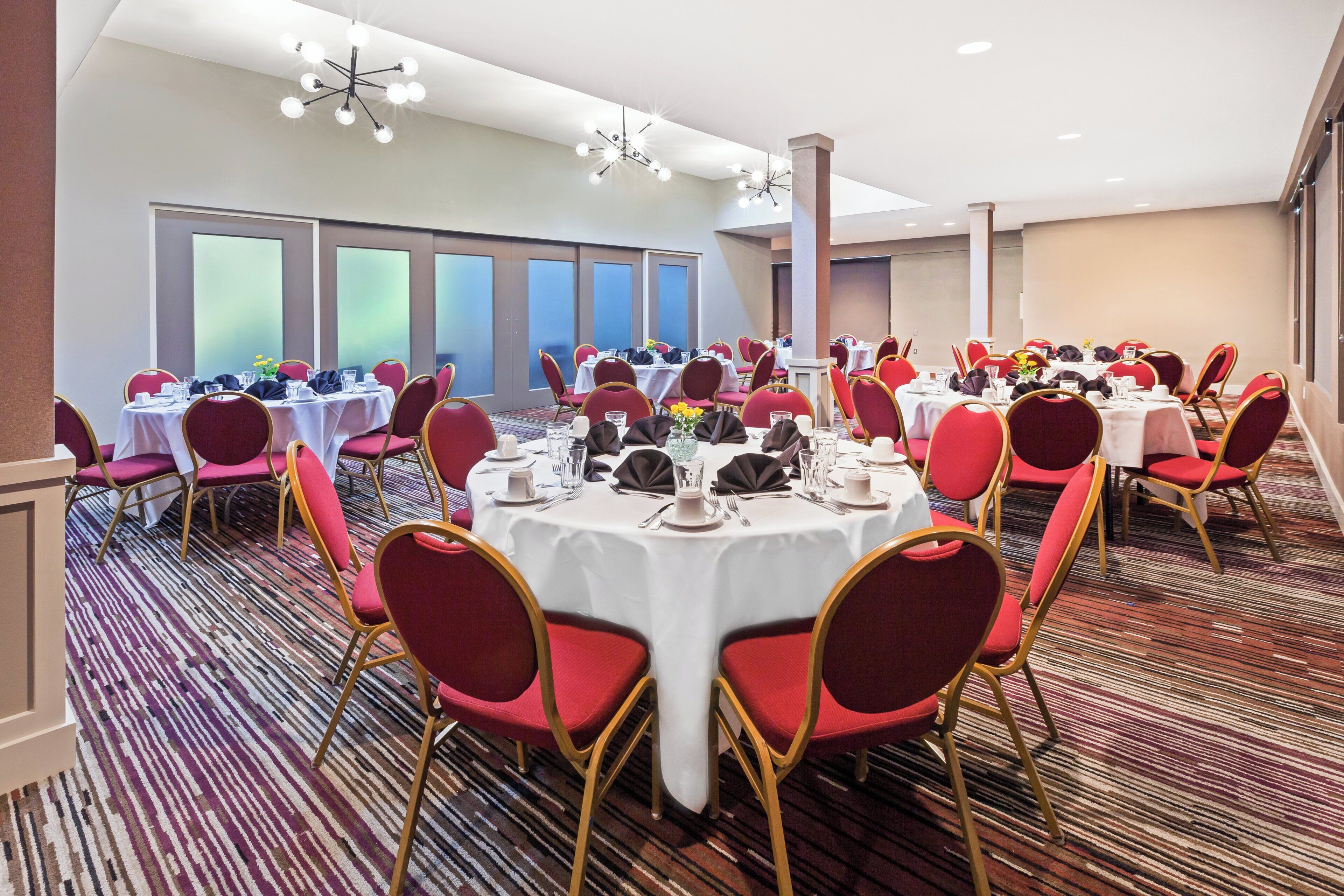 A banquet hall with round tables, red upholstered chairs, and a patterned carpet.