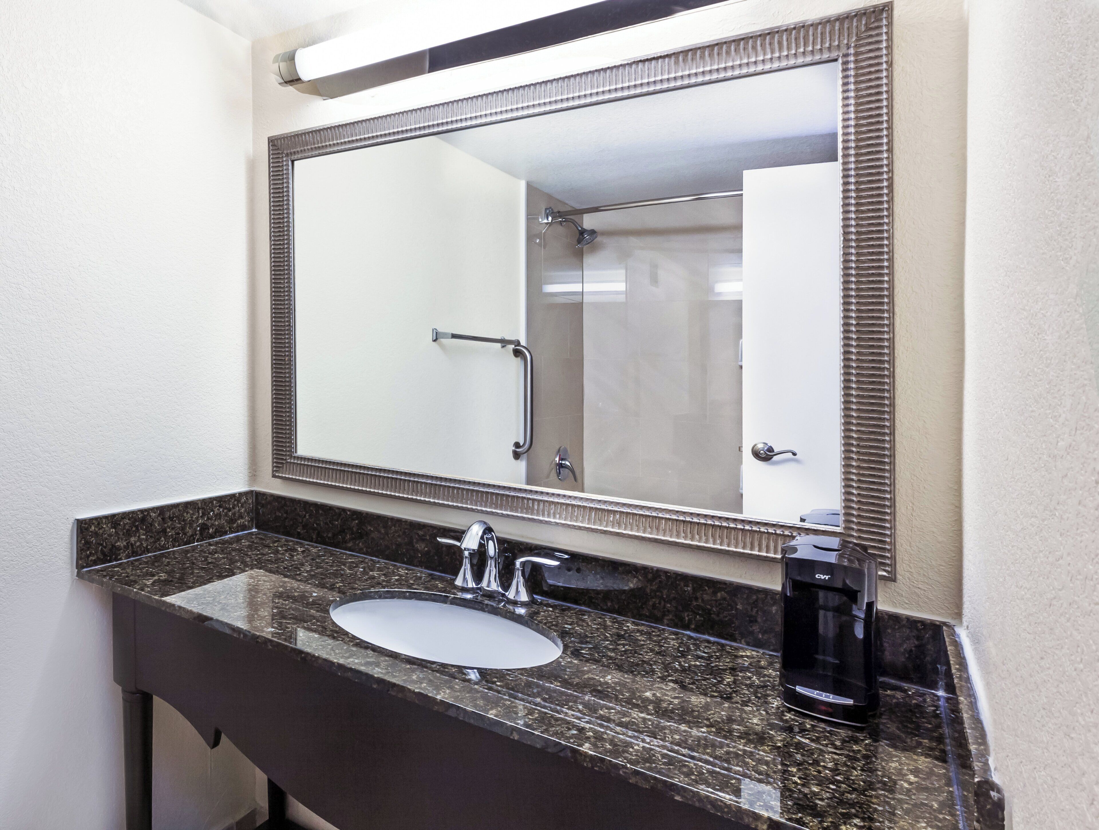 Un baño con lavamanos de mármol, un espejo grande y una cafetera.