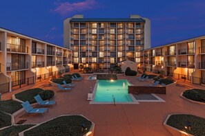 A hotel with a central pool surrounded by lounge chairs and a well-lit building facade.