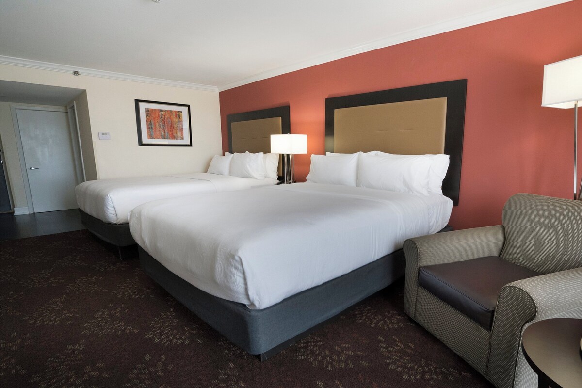 A hotel room with a large bed, a chair, a desk, and a lamp.