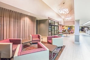 A hotel lobby with seating areas, a reception desk, and a view of the adjacent restaurant.