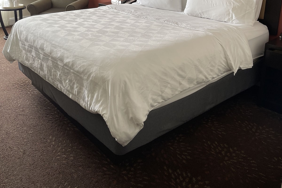 Una habitación de hotel con una cama grande, una silla, una lámpara y una mesita de noche.