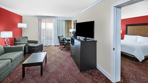 A hotel room with a red wall, a bed, a desk with a TV, a sofa, a chair, and a carpeted floor. - Holiday Inn Tyler-Conference Center by IHG (Tyler)