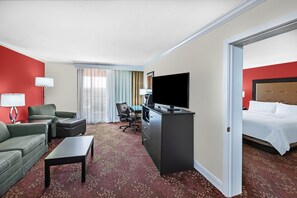 A hotel room with a red wall, a bed, a desk with a TV, a sofa, a chair, and a carpeted floor. - Holiday Inn Tyler-Conference Center by IHG (Tyler)