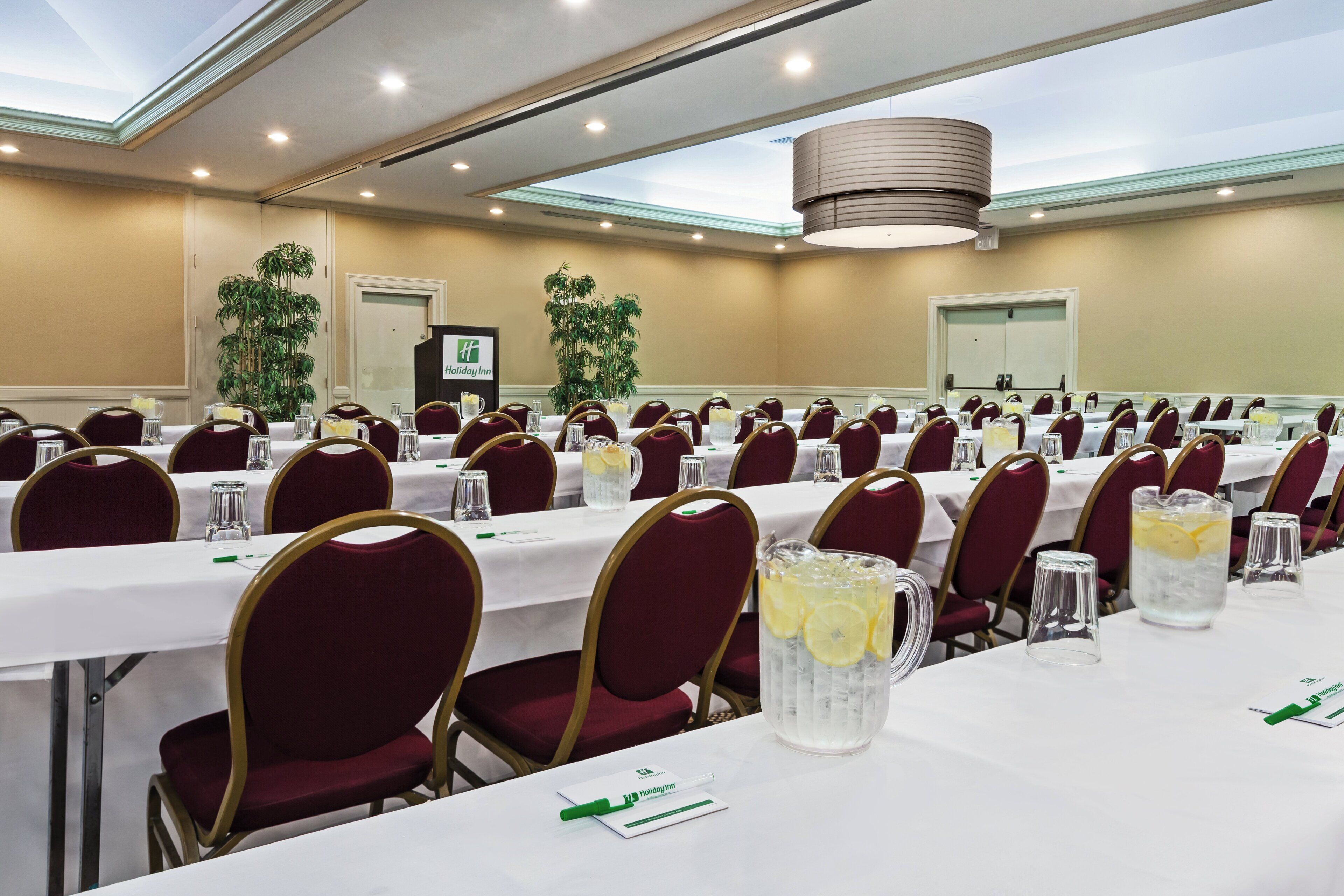 A conference room with multiple tables, chairs, and a Holiday Inn sign.