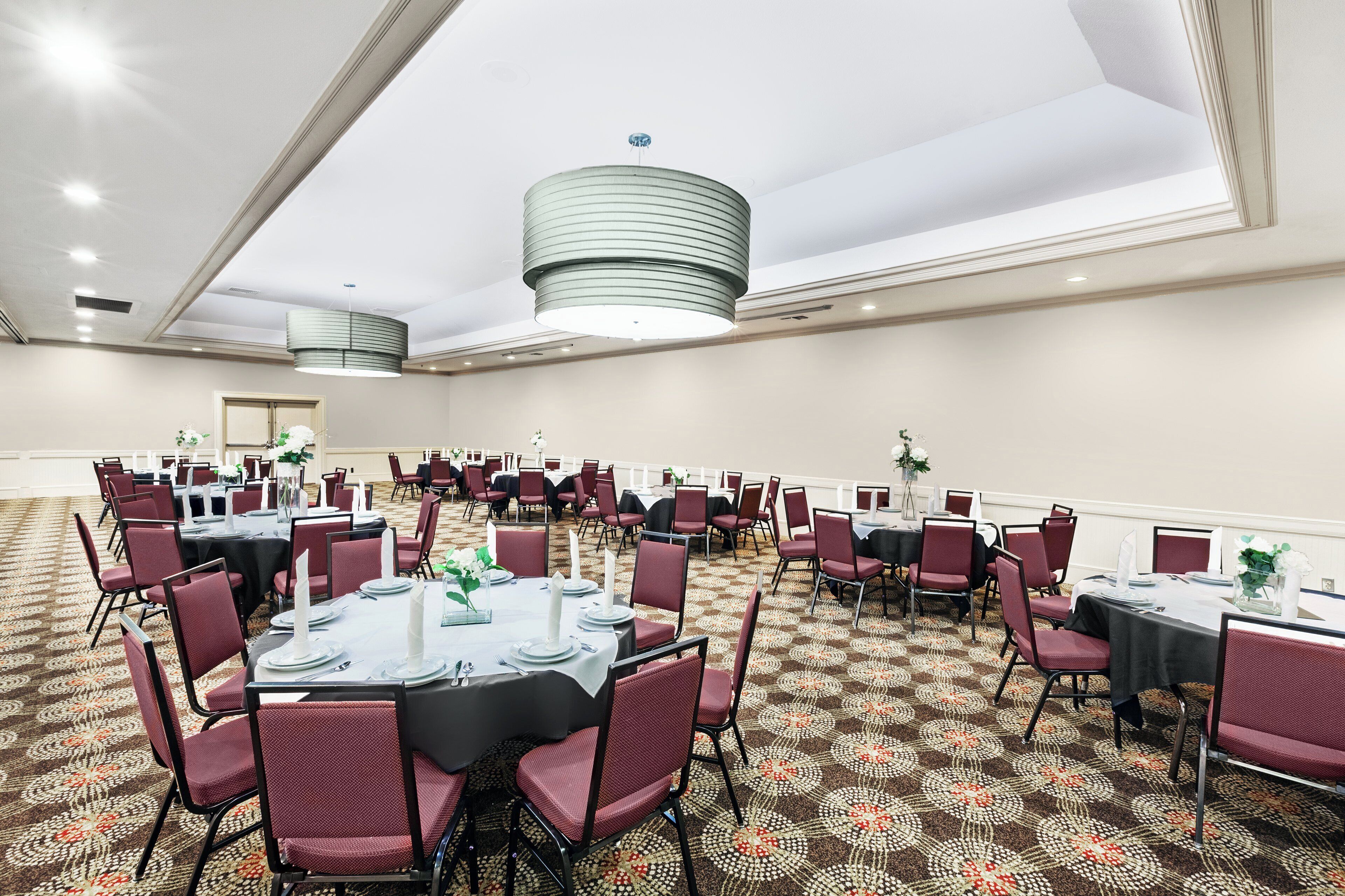 Une salle de conférence avec des tables rondes, des chaises rouges et un tapis à motifs.