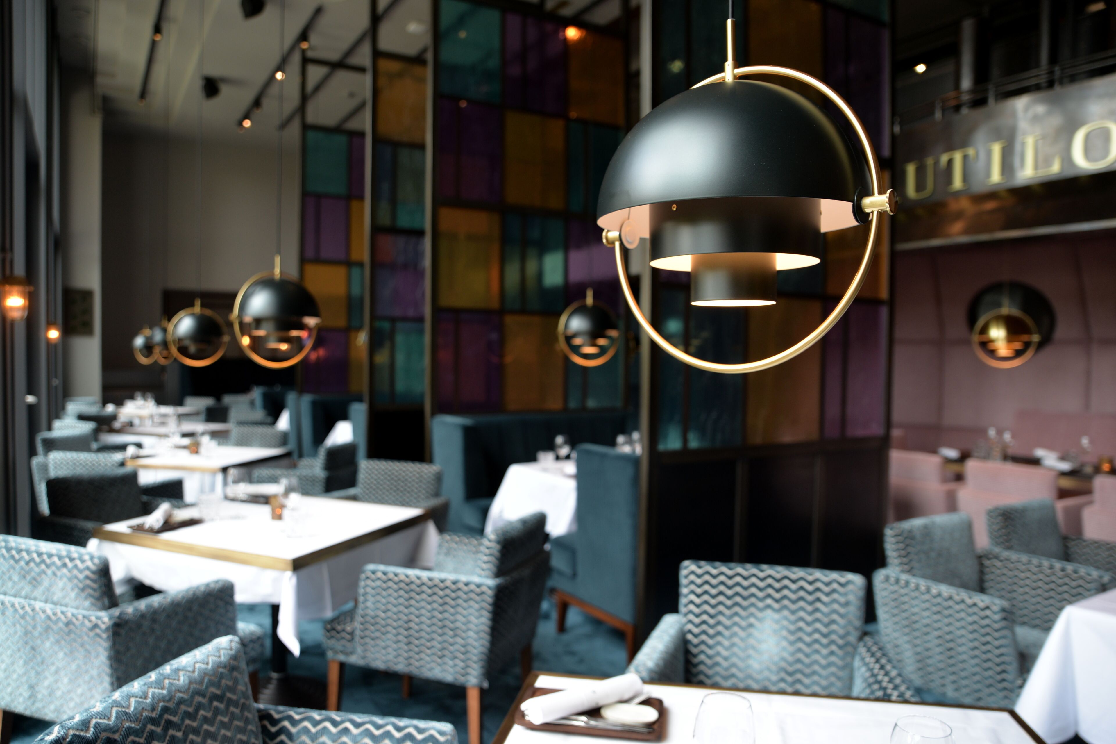 Interior de restaurante con mobiliario moderno, iluminación colgante y un letrero visible de 'UTILO'.