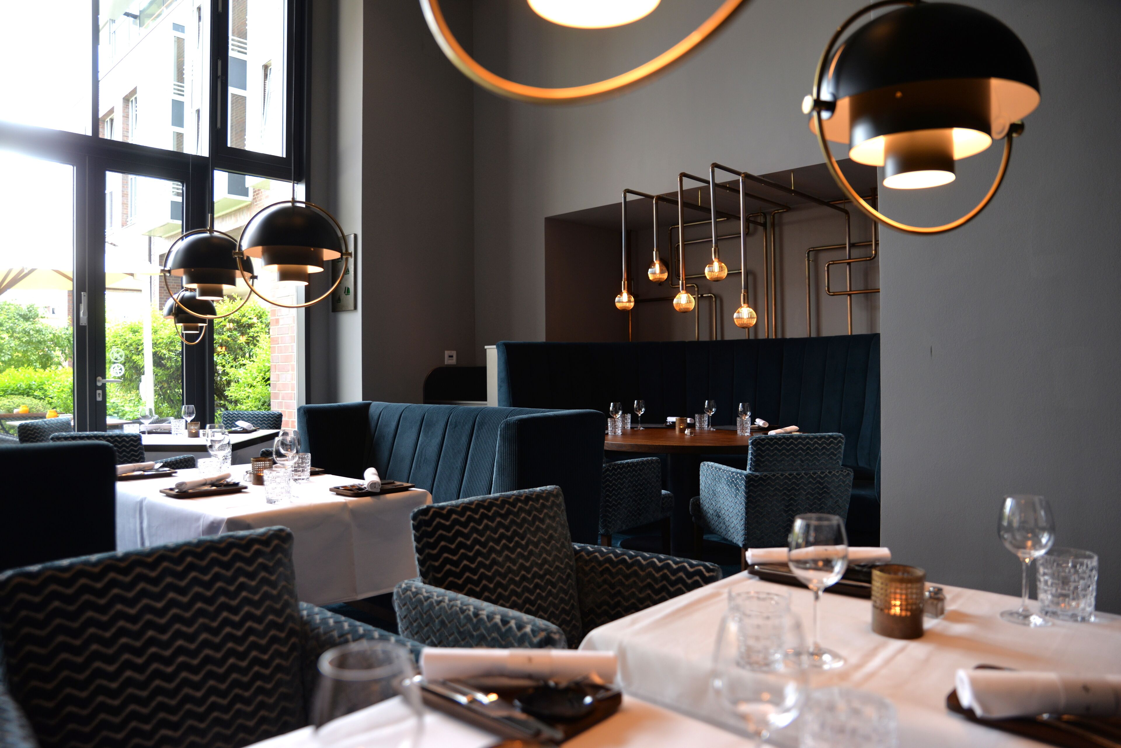 A restaurant with a modern interior, featuring dark blue upholstered seating, white tablecloths, and pendant lighting.