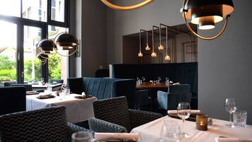 A restaurant with a modern interior, featuring dark blue upholstered seating, white tablecloths, and pendant lighting.