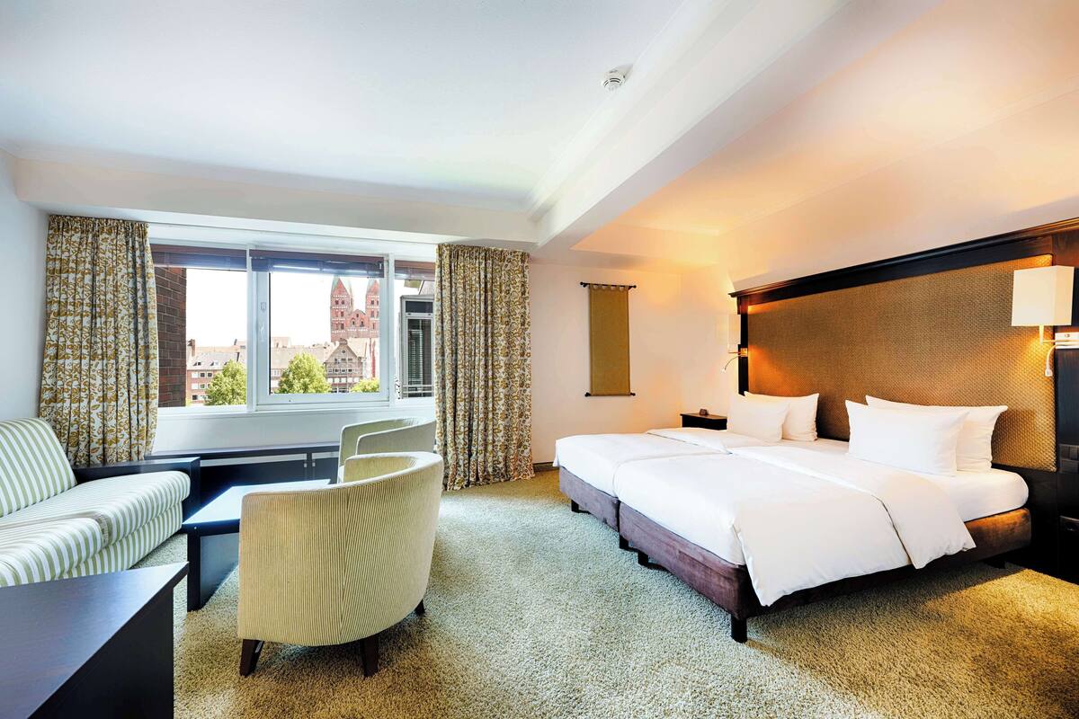 A hotel room with a bed, a sofa, a chair, and a window with curtains.