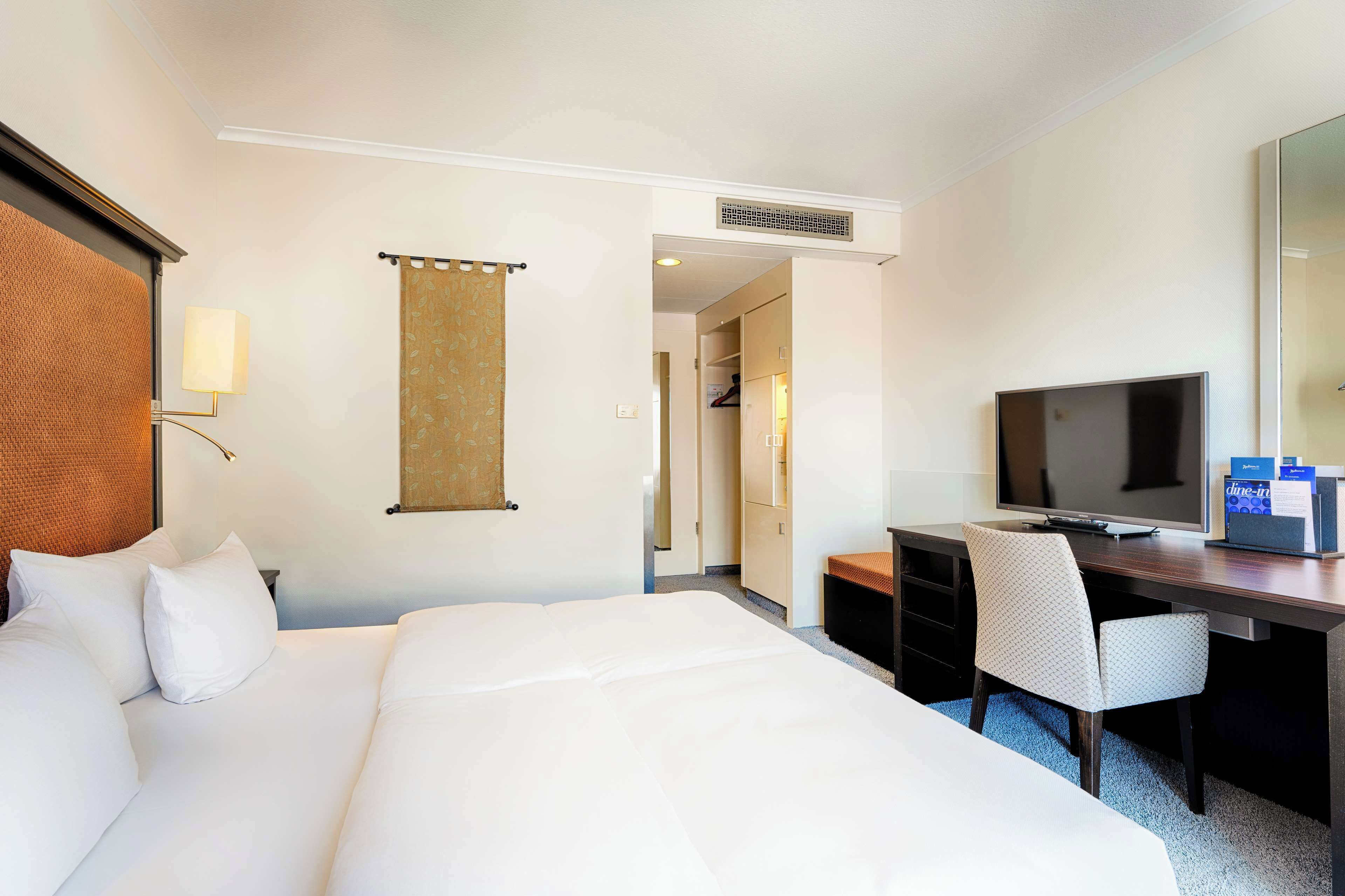Une chambre d’hôtel avec un grand lit, un bureau avec une télévision, une chaise et une armoire.