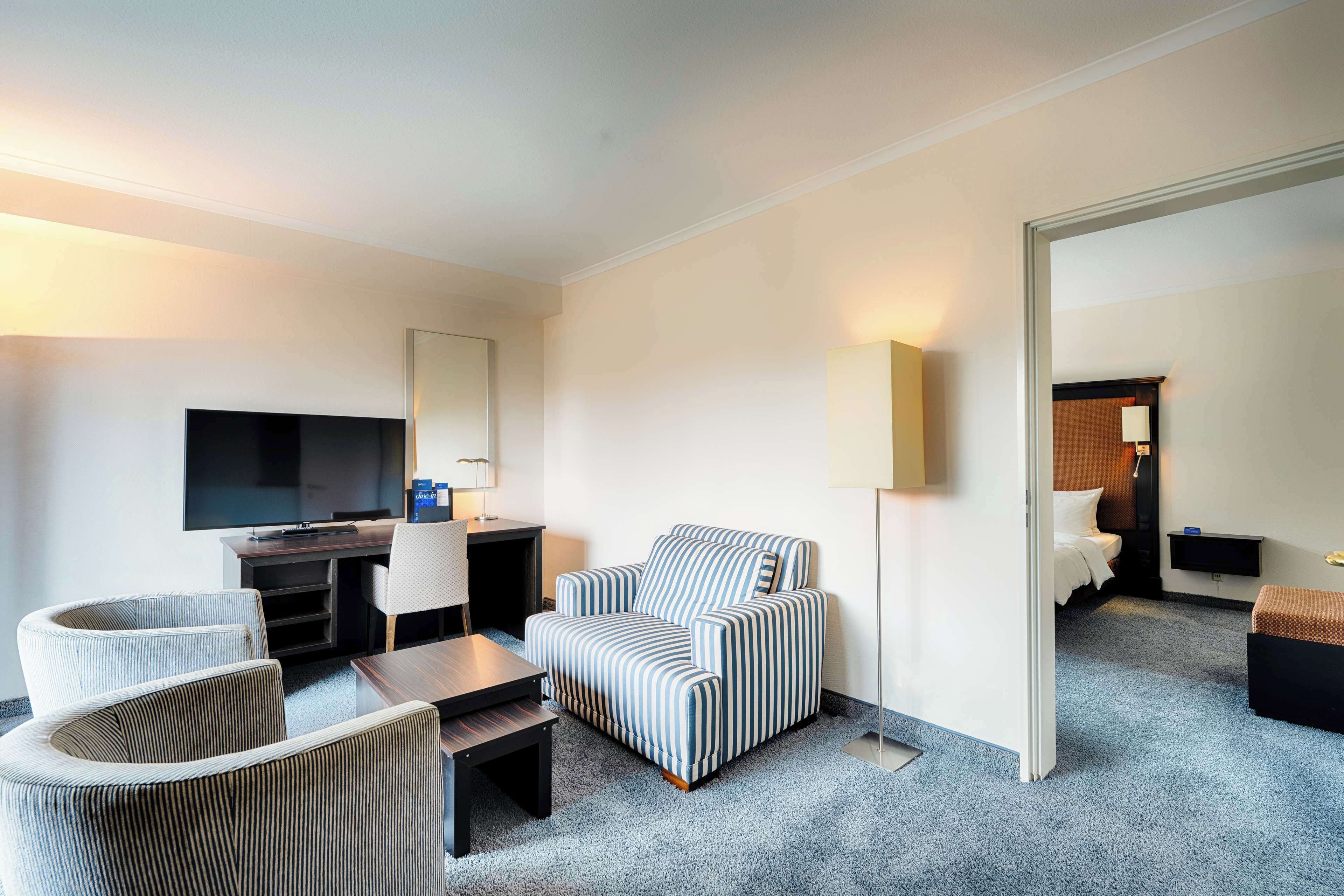 Une chambre d’hôtel équipée d’un téléviseur à écran plat, d’un fauteuil à rayures, d’un canapé, d’une petite table et d’un lit.