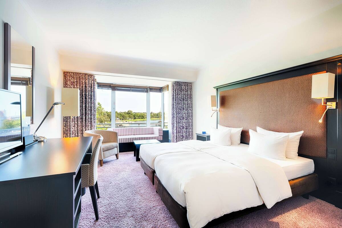 A hotel room with a large bed, a desk, a chair, a TV, and a view of the outdoors.