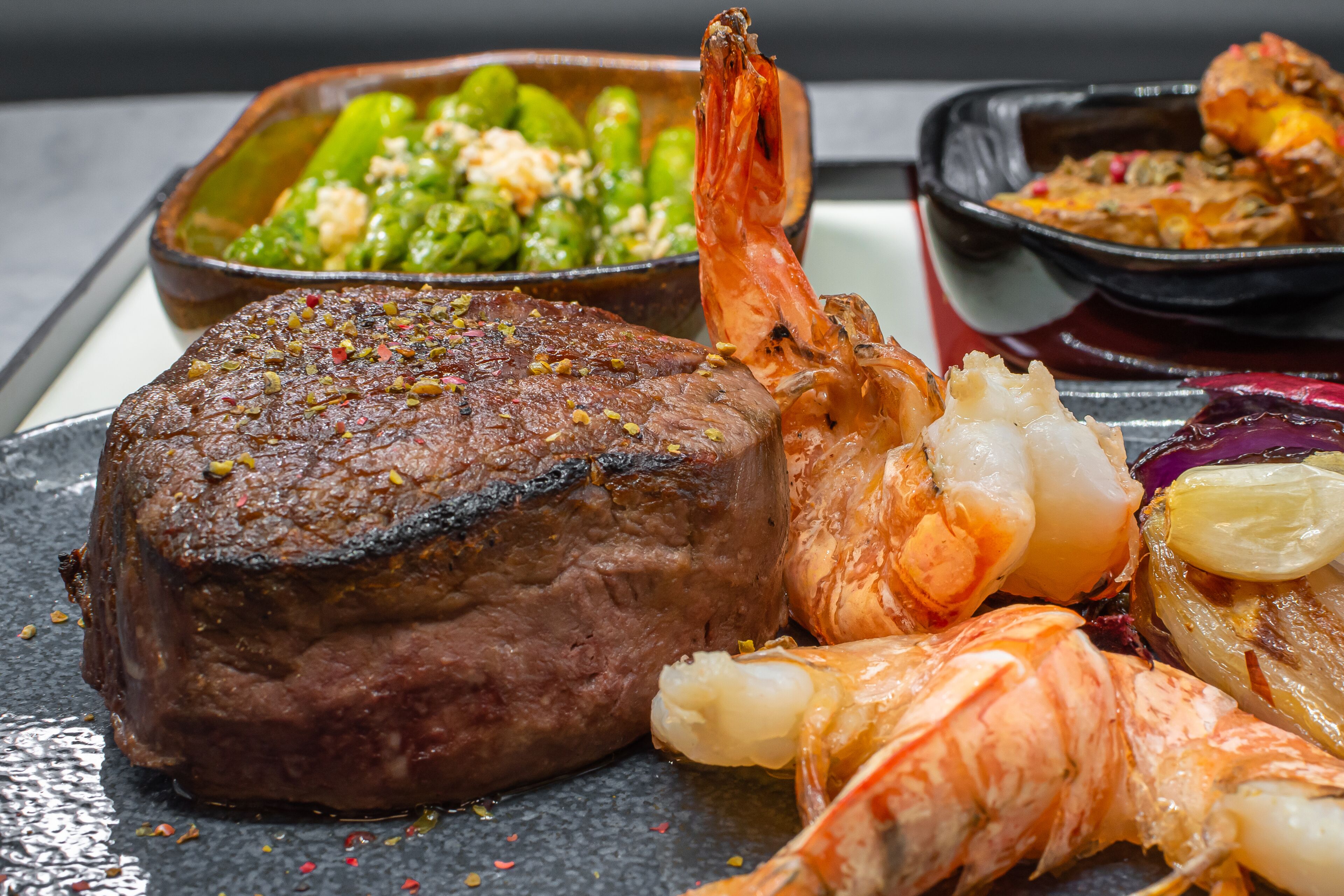 Bife, camarões e legumes em um prato.