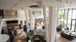 A modern hotel lobby with a central seating area, a staircase, and large windows offering views of the outdoors. - Radisson Blu Senator Hotel (Lübeck)