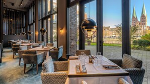 A restaurant with large windows, wicker furniture, and modern pendant lighting. - Radisson Blu Senator Hotel (Lübeck)