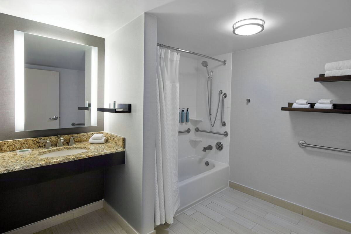 Un baño moderno con lavamanos de granito, un espejo grande, ducha con puerta de vidrio y toallero con toallas dobladas.