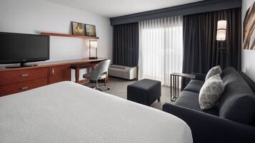 Une chambre d’hôtel avec un grand lit, un bureau doté d’un téléviseur à écran plat, un canapé et une petite table.