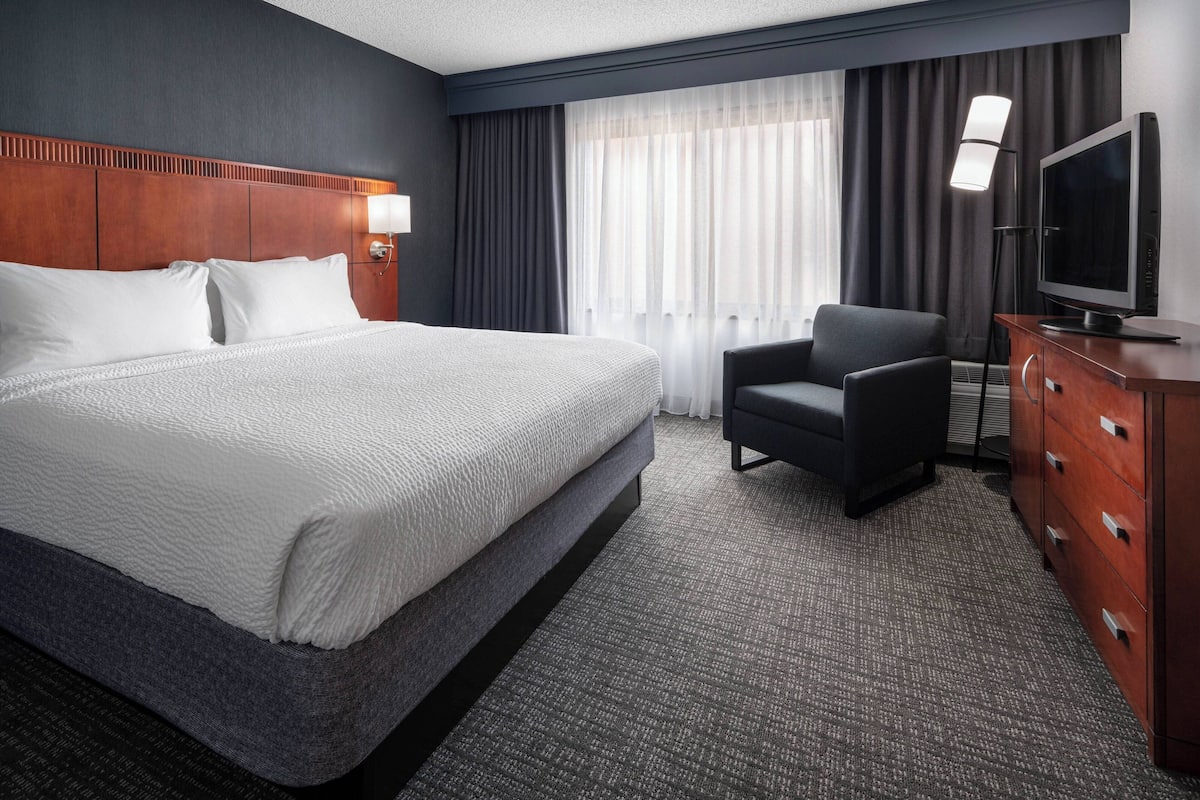 Una habitación de hotel con una cama grande, una silla, un televisor y un aparador.